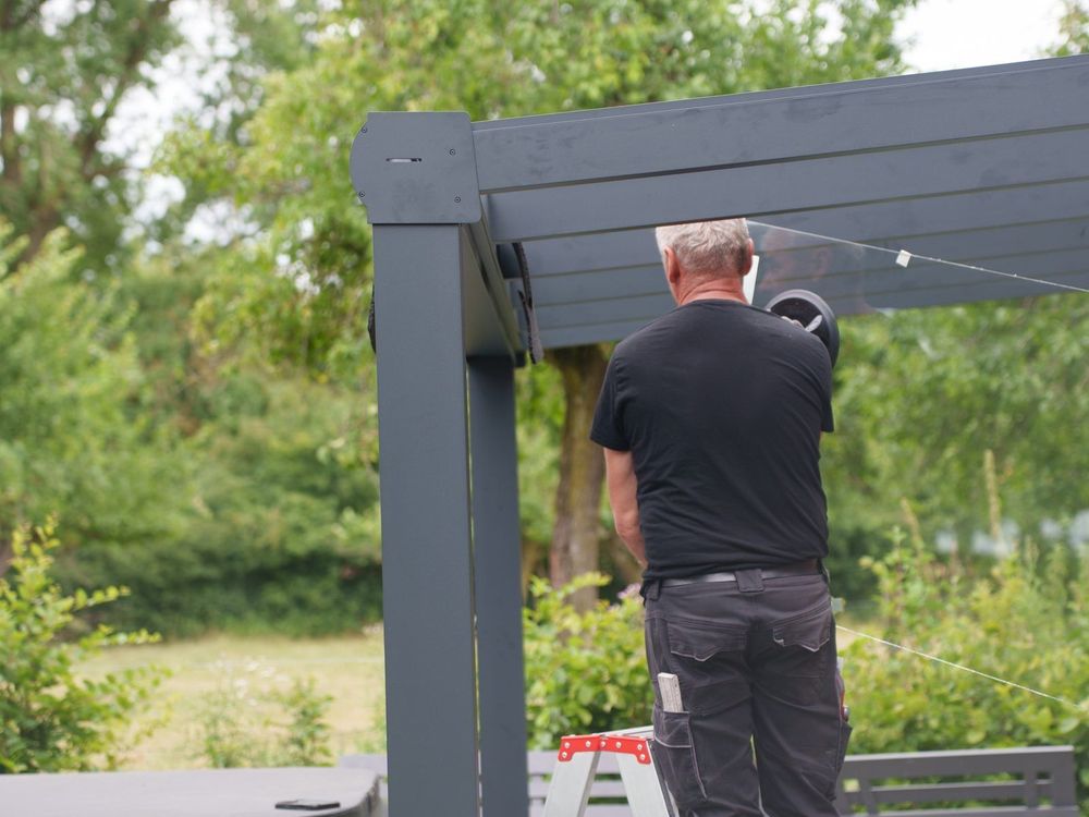 Eckpfosten und Sparren einer Terrassenüberdachung in Anthrazit, Monteur bei der Verglasung