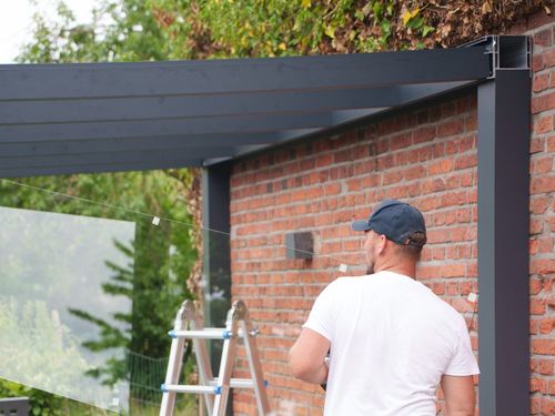 Terrassendach aus Aluminium mit ersten Glasscheiben an einer Klinkerfassade