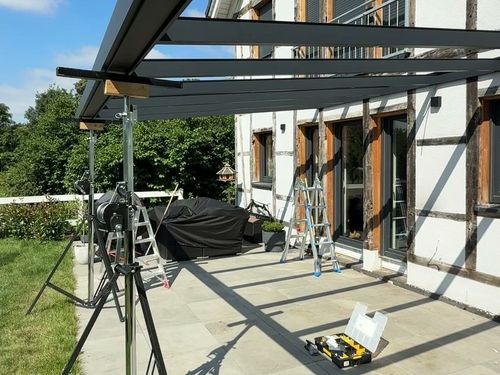 Sparren einer Aluminium-Terrassenüberdachung auf Montagestützen vor einem Fachwerkhaus